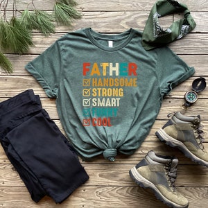 K&ouml;nnte beinhalten: Ein gr&uuml;nes T-Shirt mit dem Text "FATHER" und einer Checkliste von Eigenschaften, darunter "handsome", "strong", "smart", "funny" und "cool".