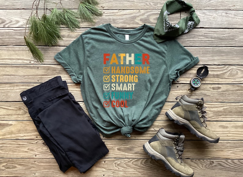 K&ouml;nnte beinhalten: Ein gr&uuml;nes T-Shirt mit dem Text "FATHER" und einer Checkliste von Eigenschaften, darunter "handsome", "strong", "smart", "funny" und "cool".
