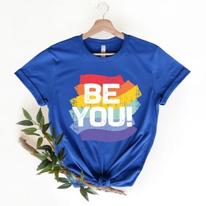 May include: A royal blue t-shirt with a rainbow-colored graphic that says "BE YOU!" in white text.