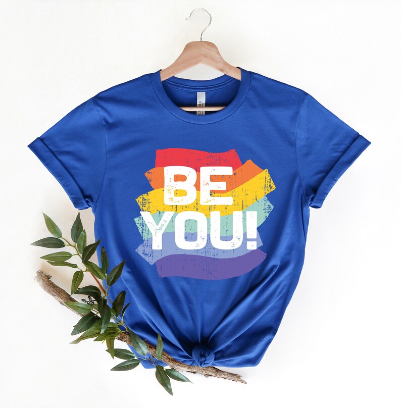 May include: A royal blue t-shirt with a rainbow-colored graphic that says "BE YOU!" in white text.