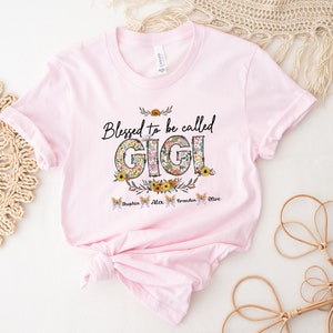May include: Pink t-shirt with the text "Blessed to be called Gigi" in black lettering with floral accents. The names "Sophia, Alex, Braden, Olive" are written in smaller font below the text.