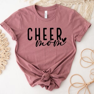 May include: A mauve t-shirt with the text "CHEER mom" in black lettering with a small heart.