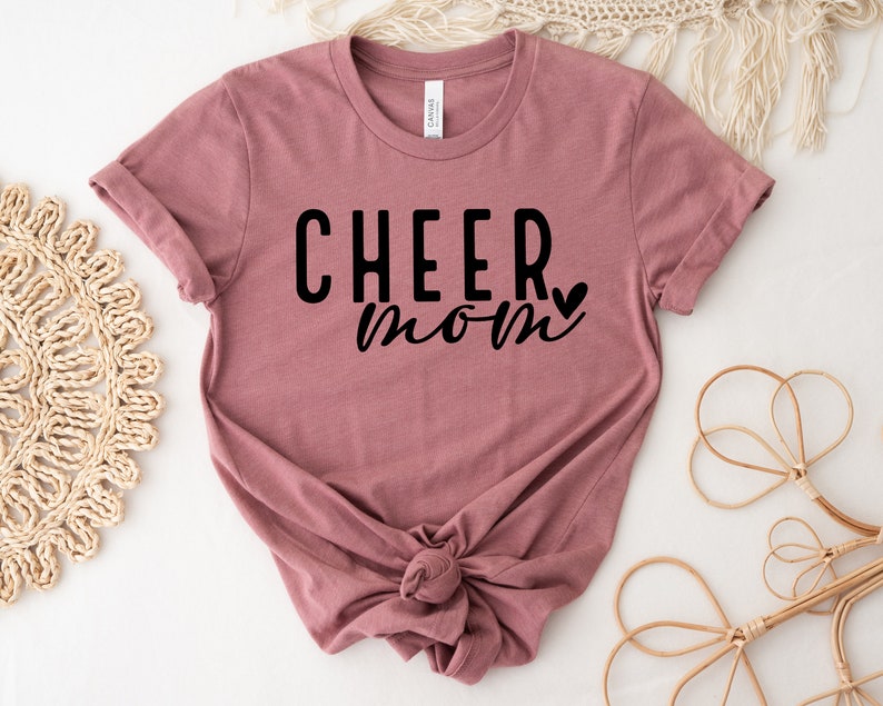 May include: A mauve t-shirt with the text "CHEER mom" in black lettering with a small heart.