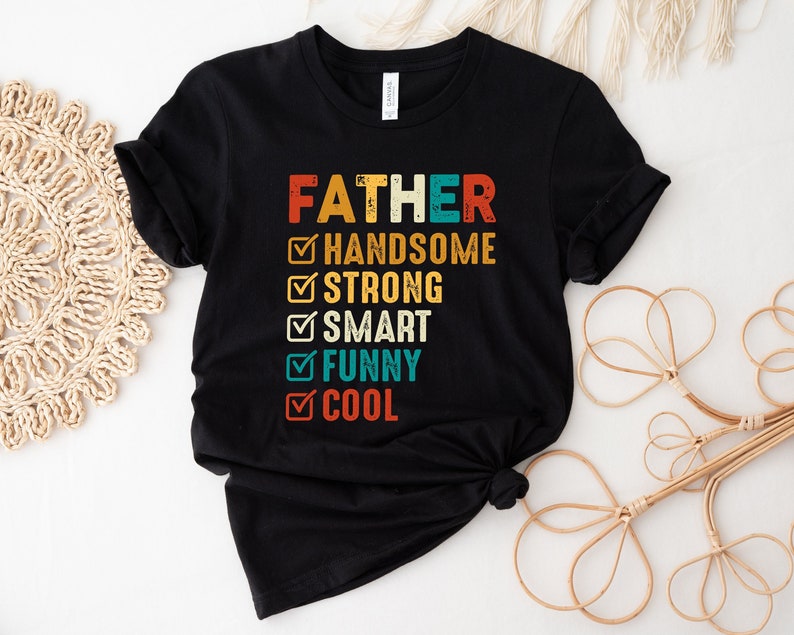 K&ouml;nnte beinhalten: Schwarzes T-Shirt mit dem Text "FATHER" in Wei&szlig; und einer Checkliste mit Eigenschaften wie "handsome", "strong", "smart", "funny" und "cool".