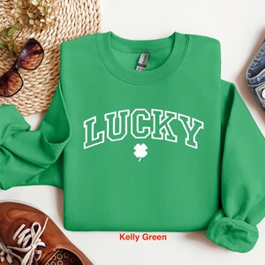 以下が含まれることがあります： ケリーグリーンのトレーナーに、白い文字で「LUCKY」と書いてあり、その下に四つ葉のクローバーがあります。