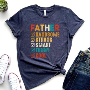 K&ouml;nnte beinhalten: Ein dunkelblaues T-Shirt mit dem Text "FATHER" in Wei&szlig; und einer Checkliste mit positiven Eigenschaften in bunter Schrift. Die Eigenschaften sind "handsome", "strong", "smart", "funny" und "cool".