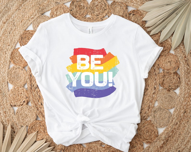 May include: White t-shirt with a rainbow-colored graphic that says "BE YOU!" in a distressed font.