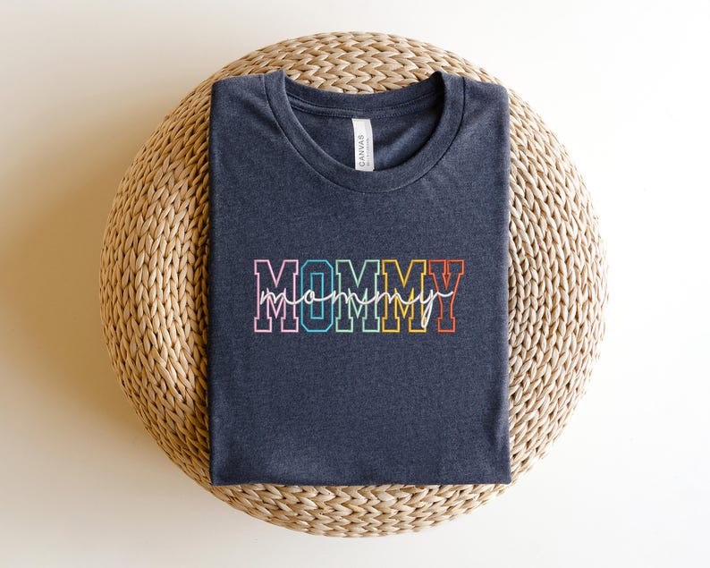 Pode incluir: Uma camiseta cinza escura com a palavra "MOMMY" em letras mai&uacute;sculas arco-&iacute;ris com um "mommy" menor escrito em cursiva abaixo.