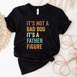 Pu&ograve; includere: Maglietta nera con una grafica in stile vintage che recita "Non &egrave; un fisico da pap&agrave;, &egrave; una figura paterna."