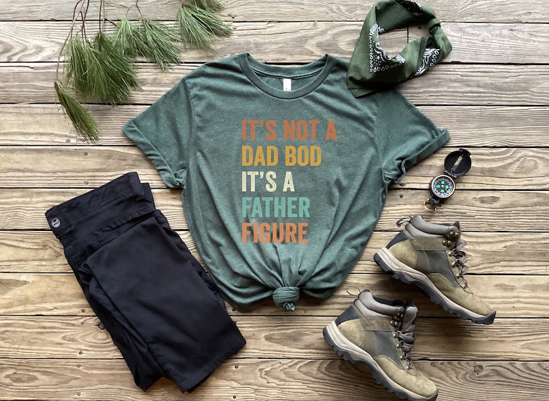 Pu&ograve; includere: Una maglietta verde con il testo "It's not a dad bod it's a father figure" in un font retr&ograve;. La maglietta &egrave; annodata ed &egrave; circondata da un paio di pantaloni neri, una bandana, una bussola e scarponi da trekking.