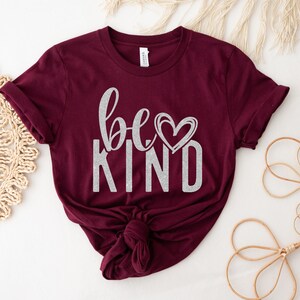 May include: Burgundy t-shirt with a silver glitter design that says "be kind" with a heart.