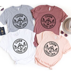 May include: Four t-shirts featuring a black and white graphic of a ship with palm trees and the text "Cousin Cruise Crew 2023". The shirts are in grey, maroon, white, and peach.