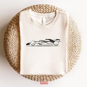 May include: A white t-shirt with a black silhouette of a racing car printed on the front. The car is facing to the right and has a black and white design.