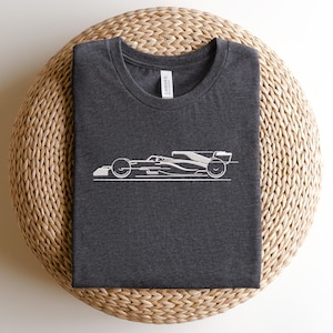 May include: A dark grey t-shirt featuring a white outline of a racing car on the front. The shirt is made from a soft, comfortable fabric.