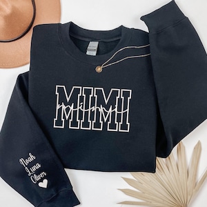 May include: Black sweatshirt with the word "MIMI" in white block letters with a white heart beat line underneath. The sleeve has the names "Noah Luna Oliver" in white with a white heart.