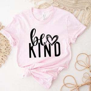 May include: Pink t-shirt with black text that reads "be kind" with a heart graphic.