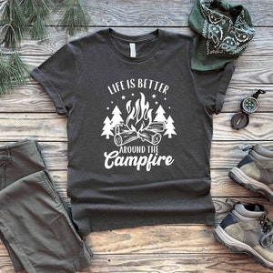 May include: A dark gray t-shirt with white text that reads "Life is better around the campfire". The text is surrounded by a campfire graphic with flames and trees.