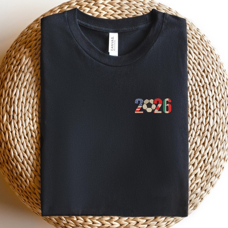 May include: Black t-shirt with a crew neck. The shirt features the number "2026" in a soccer-themed design. The "2" is in the colors of the American flag, the soccer ball is in the center, and the "6" is in the colors of the Italian flag.