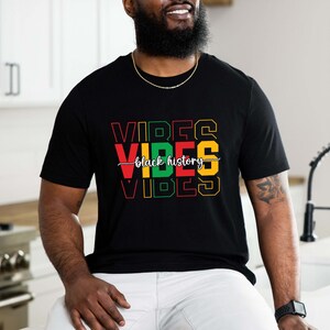 May include: Black t-shirt with the words "Vibes" in red, yellow, green, and black, with the words "Black History" written in white cursive script.