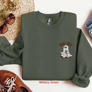 May include: A military green sweatshirt with a white ghost holding a cup of coffee and the text "Boo-Jee" on the front.