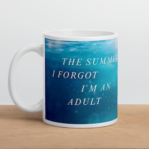 May include: White ceramic mug with a blue underwater scene and the text "THE SUMMER I FORGOT I'M AN ADULT". The mug is on a wooden surface.