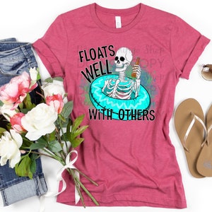 May include: A pink t-shirt featuring a skeleton wearing a blue and white inflatable ring and holding a beer. The text on the shirt reads "Floats Well With Others".