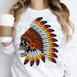 May include: A white sweatshirt with a graphic of a skull wearing a colorful Native American headdress. The headdress is made of feathers in red, yellow, white, and black.