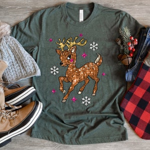 May include: A green t-shirt with a sparkly gold reindeer design. The reindeer has pink accents and is surrounded by snowflakes.
