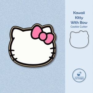 May include: A white cookie cutter shaped like Hello Kitty with a pink bow. The cutter is on a light blue background with the text "Kawaii Kitty With Bow Cookie Cutter" and a logo for Alchemy Cookie Cutters.