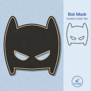 May include: A black bat mask cookie cutter set with a light brown outline. The mask has eye cutouts and pointed ears. The text "Bat Mask Cookie Cutter Set" is displayed on a light blue background.