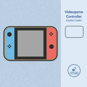 May include: A blue and red cookie cutter shaped like a video game controller. The controller has a black screen, a black button on the left side, and four black buttons on the right side. The cookie cutter is made by Alchemy Cookie Cutters.