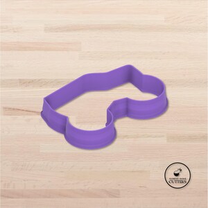 May include: A purple cookie cutter in the shape of a car. The cutter is made of plastic and has a smooth, rounded design. The Alchemy Cookie Cutters logo is in the bottom right corner.