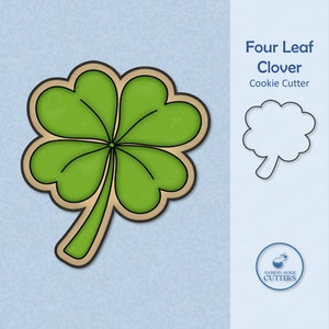 May include: A green four-leaf clover cookie cutter with a brown outline. The cutter is shaped like a traditional four-leaf clover with a stem. The text "Four Leaf Clover Cookie Cutter" is displayed above the cutter.