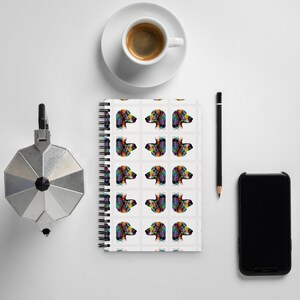 May include: A spiral bound notebook with a white background and a repeating pattern of colorful dachshund dog illustrations. Each dog is depicted in a different color combination, with a rainbow-like effect.