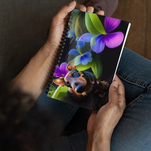 May include: A spiral bound notebook with a colorful illustration of a puppy with purple and blue flowers. The puppy is brown and black with a white chest and a pink nose.