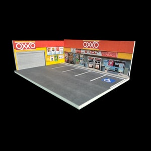 May include: A miniature model of an OXXO convenience store with a red and yellow facade, a gray parking lot, and a blue handicapped parking sign.