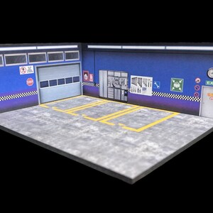 May include: A blue and grey diorama of a garage with a roll-up door, a side door labeled "EXIT", and yellow lines on the floor.