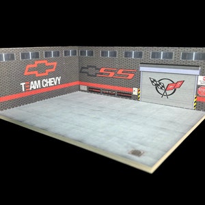 May include: A model garage diorama with a brick wall backdrop. The wall features a red and white Chevrolet logo with the text "TEAM CHEVY" and a red and white "SS" logo. The garage door has a red and white Corvette logo with the text "Corvette" and a red "STOP" sign.
