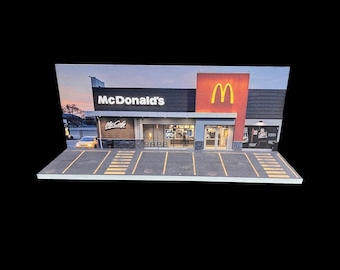 Puede incluir: Un modelo de un restaurante McDonald's con un logotipo 'M' amarillo en la fachada. El edificio es de madera y tiene un aparcamiento delante.