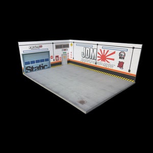 May include: A white diorama of a garage with a gray concrete floor. The garage has a large roll-up door with the word "Static" printed on it. The back wall has the words "JDM Japanese Domestic Market" printed on it with a red and white rising sun graphic.