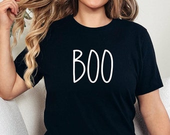 May include: A black t-shirt with the word "BOO" written in white on the front. The shirt is being worn by a person with long blonde hair and blue jeans.