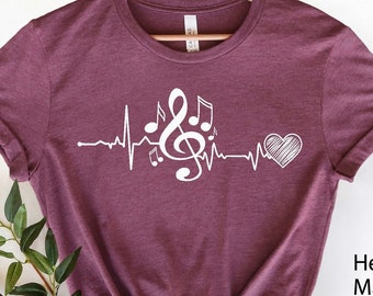 Puede incluir: Camiseta color granate con un diseño de latido de corazón musical blanco. El diseño incluye una clave de sol, notas musicales y un corazón. El texto "Heather Maroon" es visible en la esquina inferior derecha.