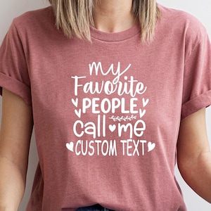 May include: A mauve t-shirt with white text that reads "my favorite people call me CUSTOM TEXT" with hearts and a small floral design.