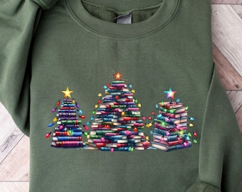Op de afbeelding: Militairgroen sweatshirt met een afbeelding van drie kerstbomen gemaakt van boeken. Elke boom is versierd met kleurrijke lichtjes en bekroond met een ster. De tekst "MILITARY GREEN" staat onderaan.