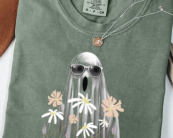 Op de afbeelding: Een mosgroen t-shirt met een spook met een zonnebril en bloemen. Het shirt heeft een Comfort Colors label en een zilveren ketting met een hanger. Het woord "MOSS" staat onderaan gedrukt.