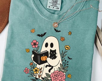 May include: Light green t-shirt with a graphic of a ghost reading a book with a black cat, surrounded by flowers and bats. The shirt has a crew neck and short sleeves. The text "LIGHT GREEN" is at the bottom of the image.
