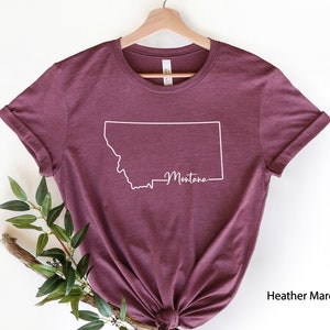 May include: A heather maroon t-shirt with a white outline of the state of Montana and the word "Montana" written inside the outline.