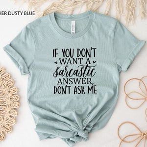 May include: A light blue t-shirt with the text "If you don't want a sarcastic answer, don't ask me" in black lettering.