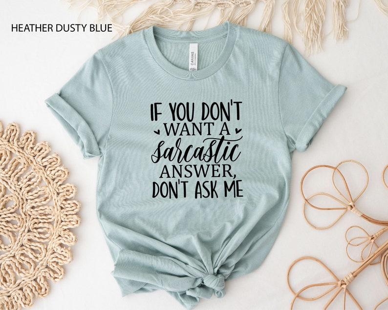 May include: A light blue t-shirt with the text "If you don't want a sarcastic answer, don't ask me" in black lettering.