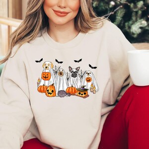 May include: A white sweatshirt with a graphic of five dogs dressed as ghosts holding pumpkins and candy. The dogs are a golden retriever, a pug, a french bulldog, a chihuahua, and a terrier. The sweatshirt is a light cream color and has a crew neck.